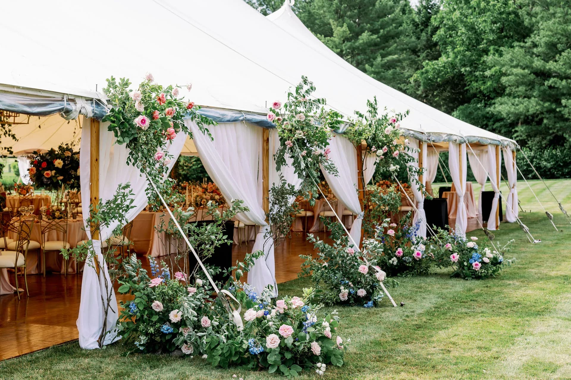 Elegant tented wedding reception with floral arches on a green New England lawn